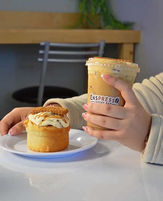 Persona sosteniendo un latte lotus helado junto a un rol de lotus en Enspresso